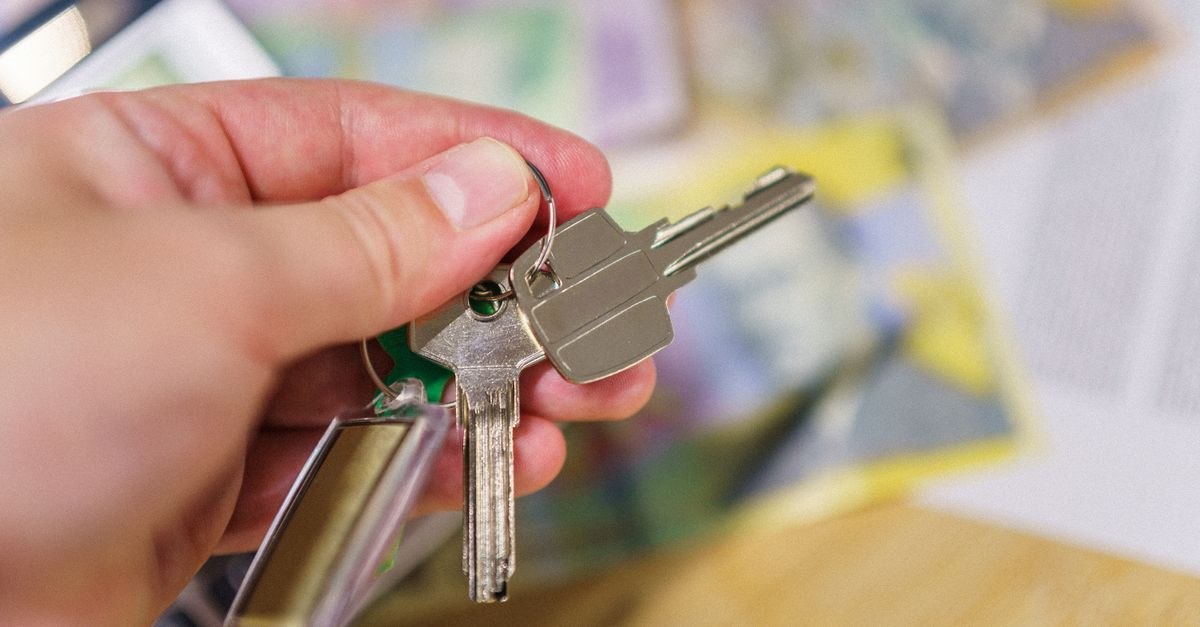 Крупный план ключей в руке, представляющих право собственности, с размазанными финансовыми документами на заднем плане.